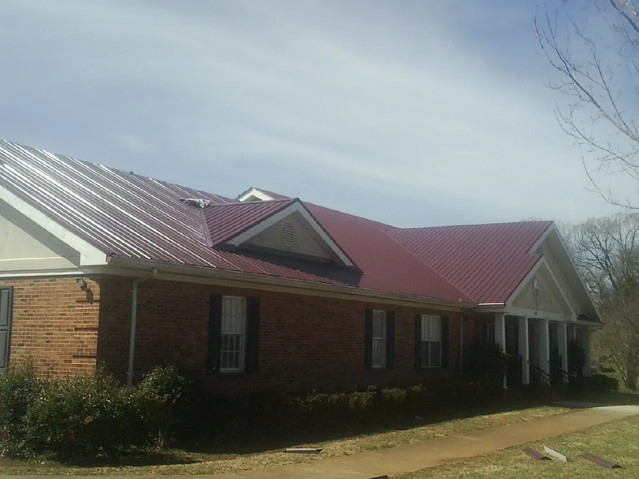 Red metal roof with gabled entries on a long brick building, from a Hail Damage Roof Repair job in Harvard
