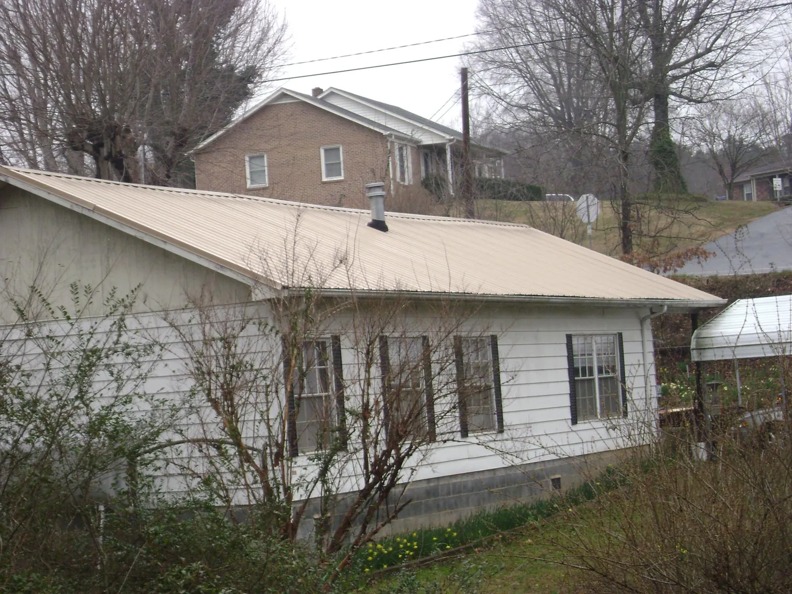 Tan metal roof on a white sided house set into a hillside — Commercial Roofing by Roofing Brothers in Harvard